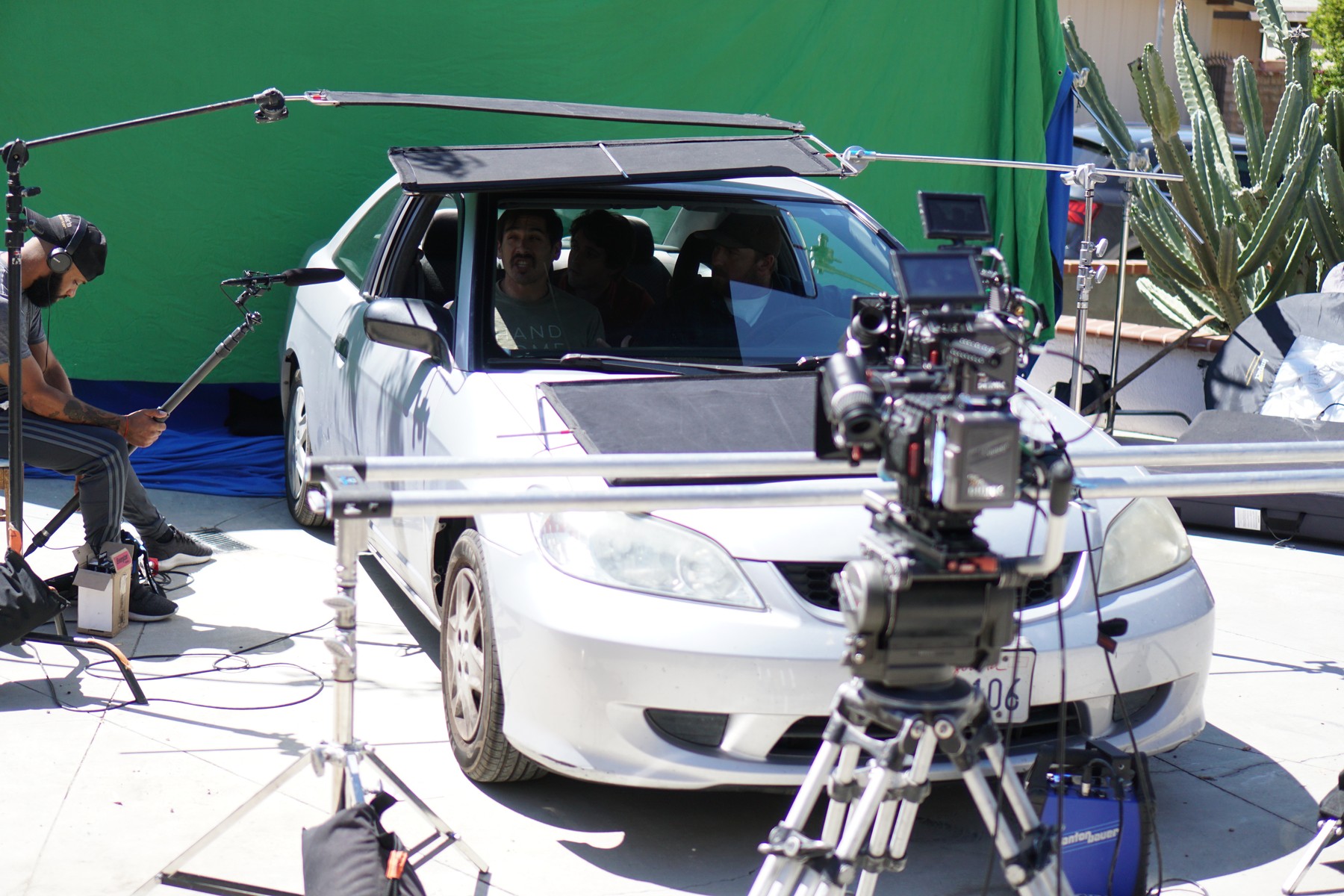 Car scene photographed against a green screen with camera and lighting rigs